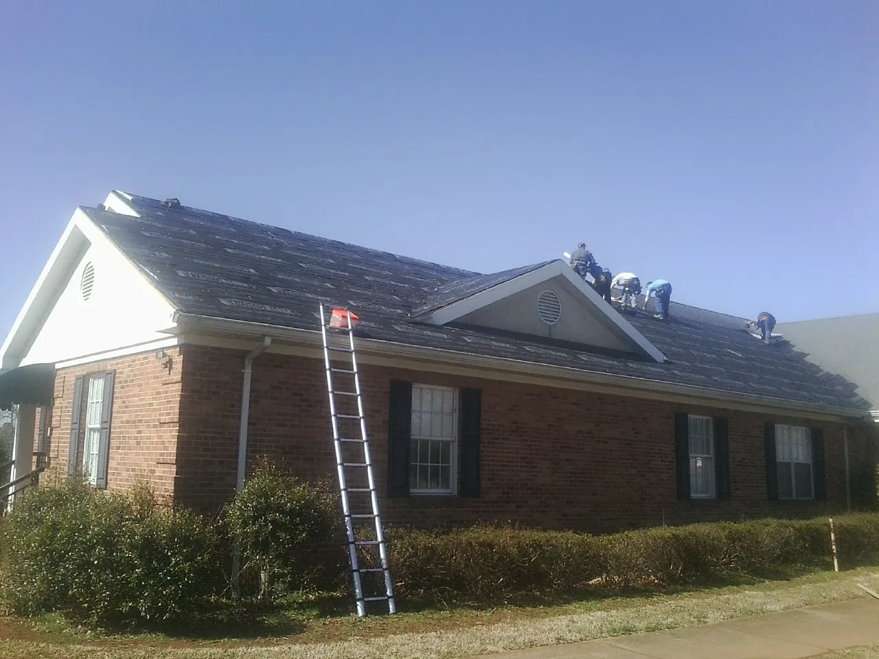Crew tearing shingles off a brick ranch roof with a ladder set — Emergency Roof Repair work by our crew in Thomaston