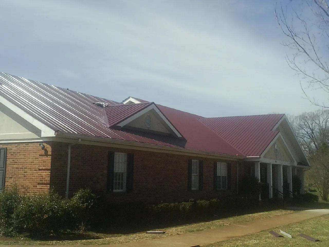Red metal roof with gabled entries on a long brick building, from a Hail Damage Roof Repair job in Thomaston