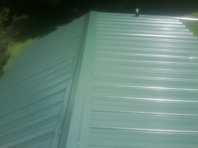 New green metal panels meeting at the ridge of a roof — Flat Roof Repair work by our crew in Thomaston